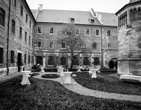 Historischer Innenhof mit Stehtischen und Bogenfenstern in schwarz-weißer Aufnahme.