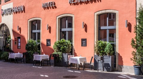 Gedeckte Tische stehen unter dem Schriftzug an der Hausfassade des Restaurants.
