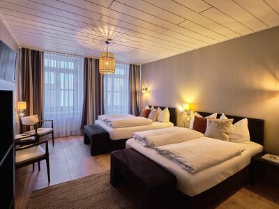 Hotelzimmer mit zwei Doppelbetten auf modernem Holzboden, Komode und Teppich.