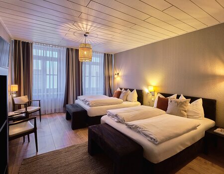 Hotelzimmer mit zwei Doppelbetten auf modernem Holzboden, Komode und Teppich.