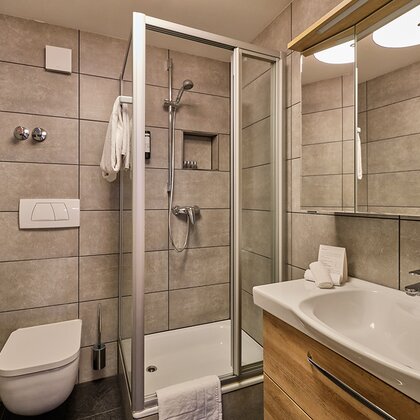 Badezimmer mit Dusche, WC, grauen, großen Fliesen und frischen Handtüchern.