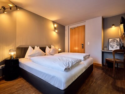 Hotelzimmer mit Doppelbett, Holzboden, Sitznische und Holztüre.